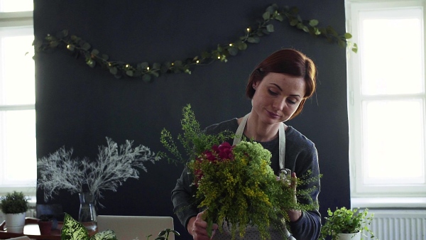 A young creative woman arranging flowers in a flower shop. A startup of florist business. Slow motion.