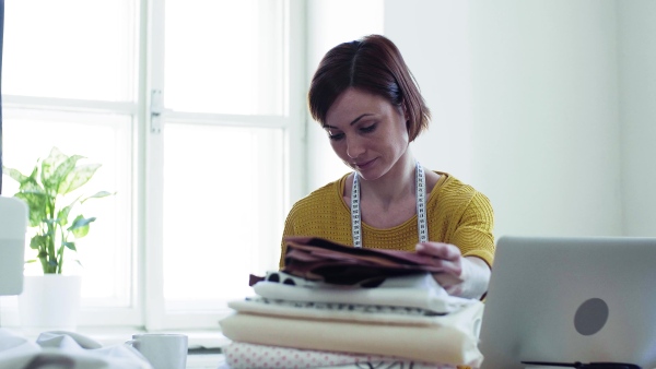 Young creative woman with laptop working in a studio, startup of small tailoring business.