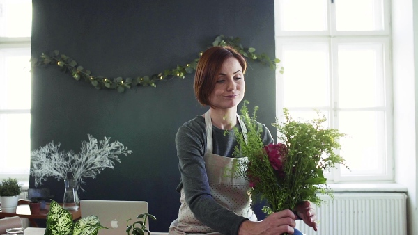 A young creative woman arranging flowers in a flower shop. A startup of florist business. Slow motion.