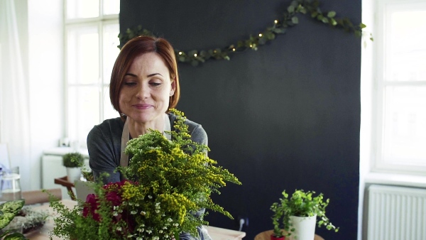 A young creative woman arranging flowers in a flower shop. A startup of florist business. Slow motion.