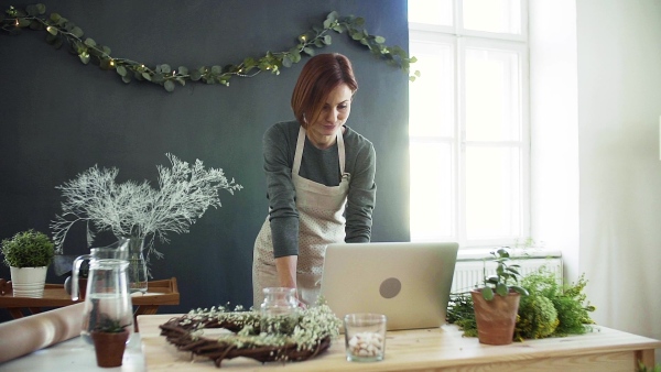 A young creative woman arranging flowers in a flower shop, using laptop. A startup of florist business. Slow motion.