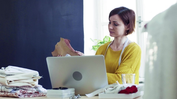 Young creative woman with laptop working in a studio, startup of small tailoring business.