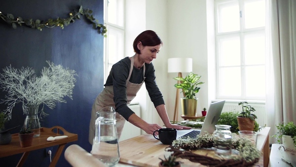 A young creative woman arranging flowers in a flower shop, using laptop. A startup of florist business. Slow motion.