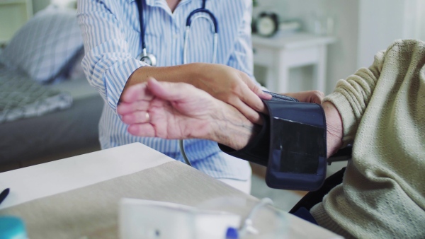 An unrecognizable young health visitor measuring a blood pressure of a senior woman at home.