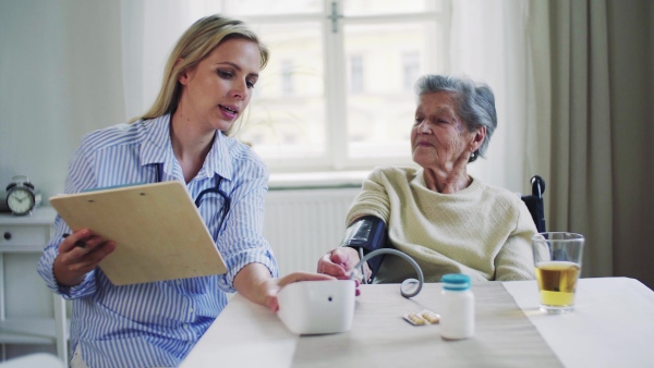 A young health visitor measuring a blood pressure of a senior woman at home.