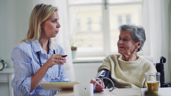 A young health visitor measuring a blood pressure of a senior woman at home.