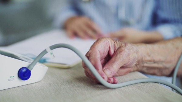 An unrecognizable young health visitor measuring a blood pressure of a senior woman at home, a midsection.