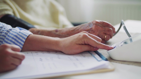 A midsection of health visitor measuring a blood pressure of a senior woman at home.