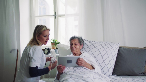 A young health visitor helping a happy sick senior woman in bed at home.