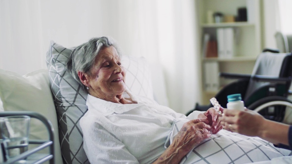 A health visitor giving pills to a sick senior woman lying in bed at home.