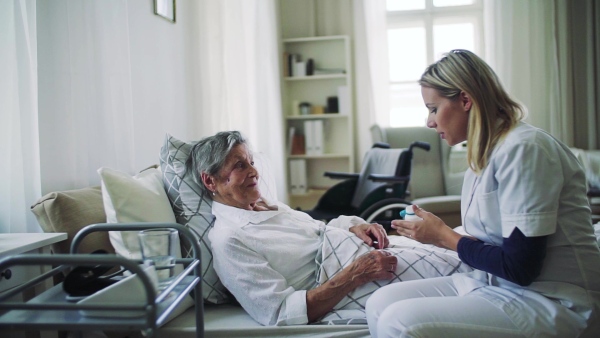 A health visitor giving pills to a sick senior woman lying in bed at home. Slow motion.