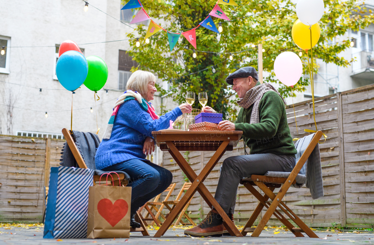 Portrait of happy senior couple with wine in outdoor cafe in city, celebrating birthday.