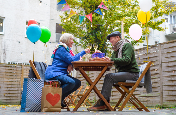 Portrait of happy senior couple with wine in outdoor cafe in city, celebrating birthday.