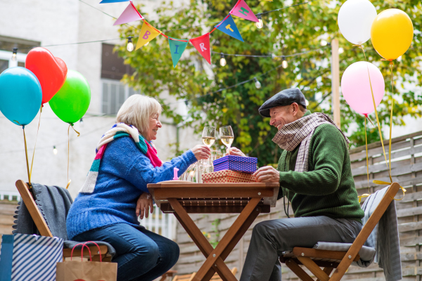 Portrait of happy senior couple with wine in outdoor cafe in city, celebrating birthday.