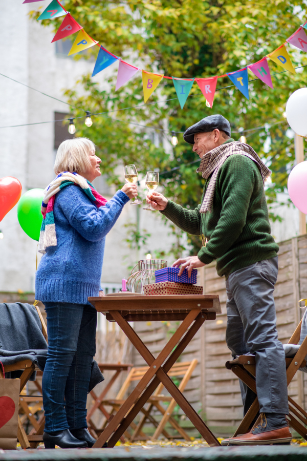 Portrait of happy senior couple with wine in outdoor cafe in city, celebrating birthday.