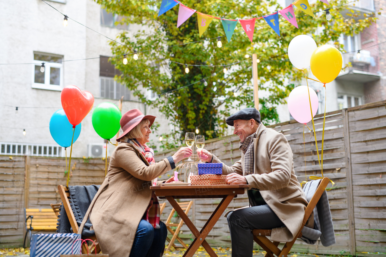 Portrait of happy senior couple with wine in outdoor cafe in city, celebrating birthday.