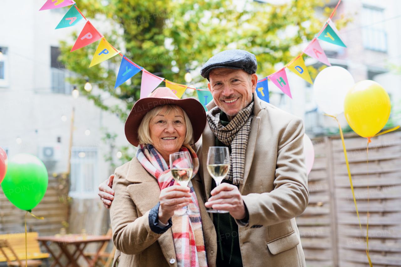 Portrait of happy senior couple with wine in outdoor cafe in city, celebrating birthday.