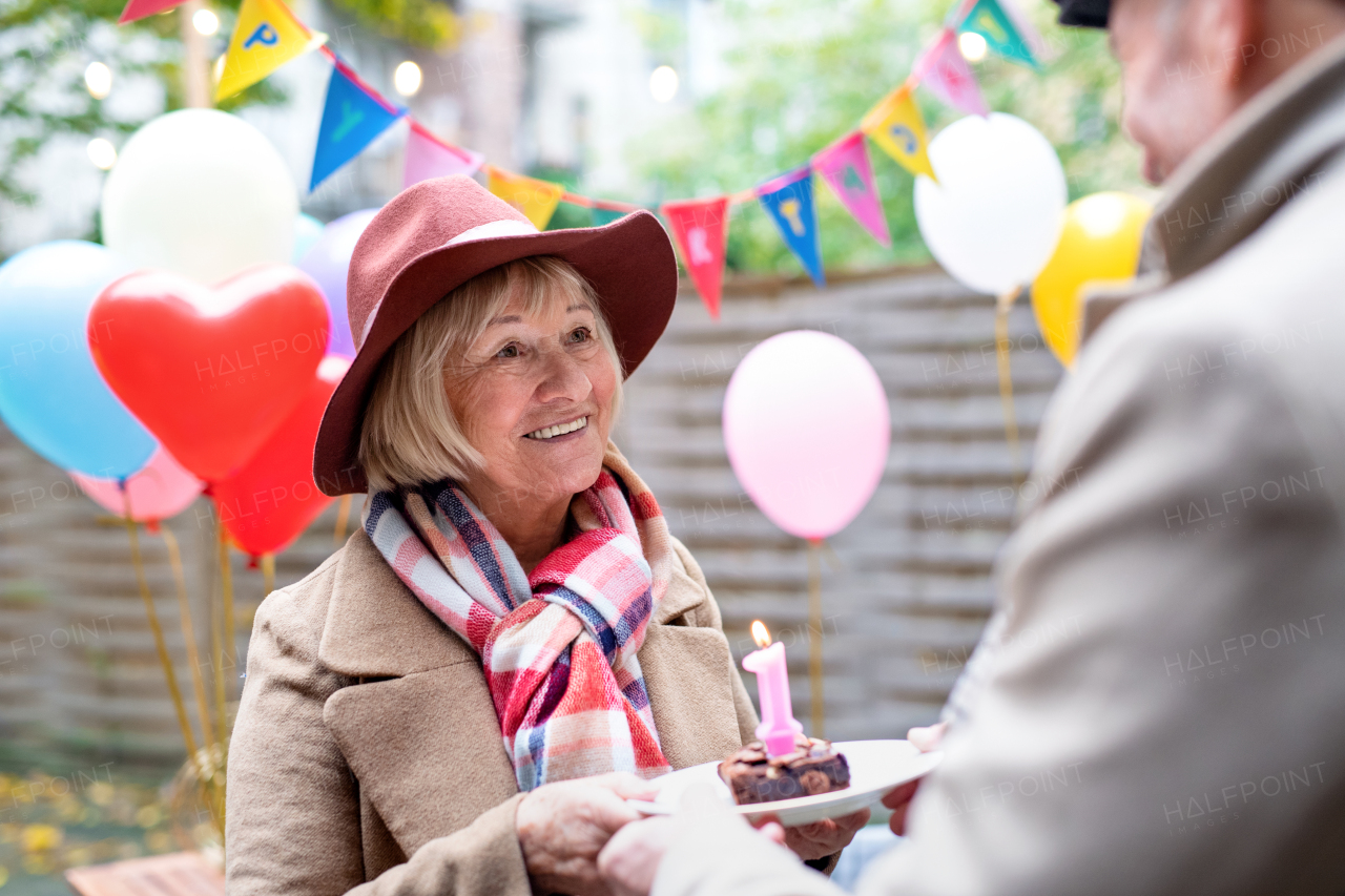 Portrait of happy senior couple with cake in outdoor cafe in city, celebrating birthday.