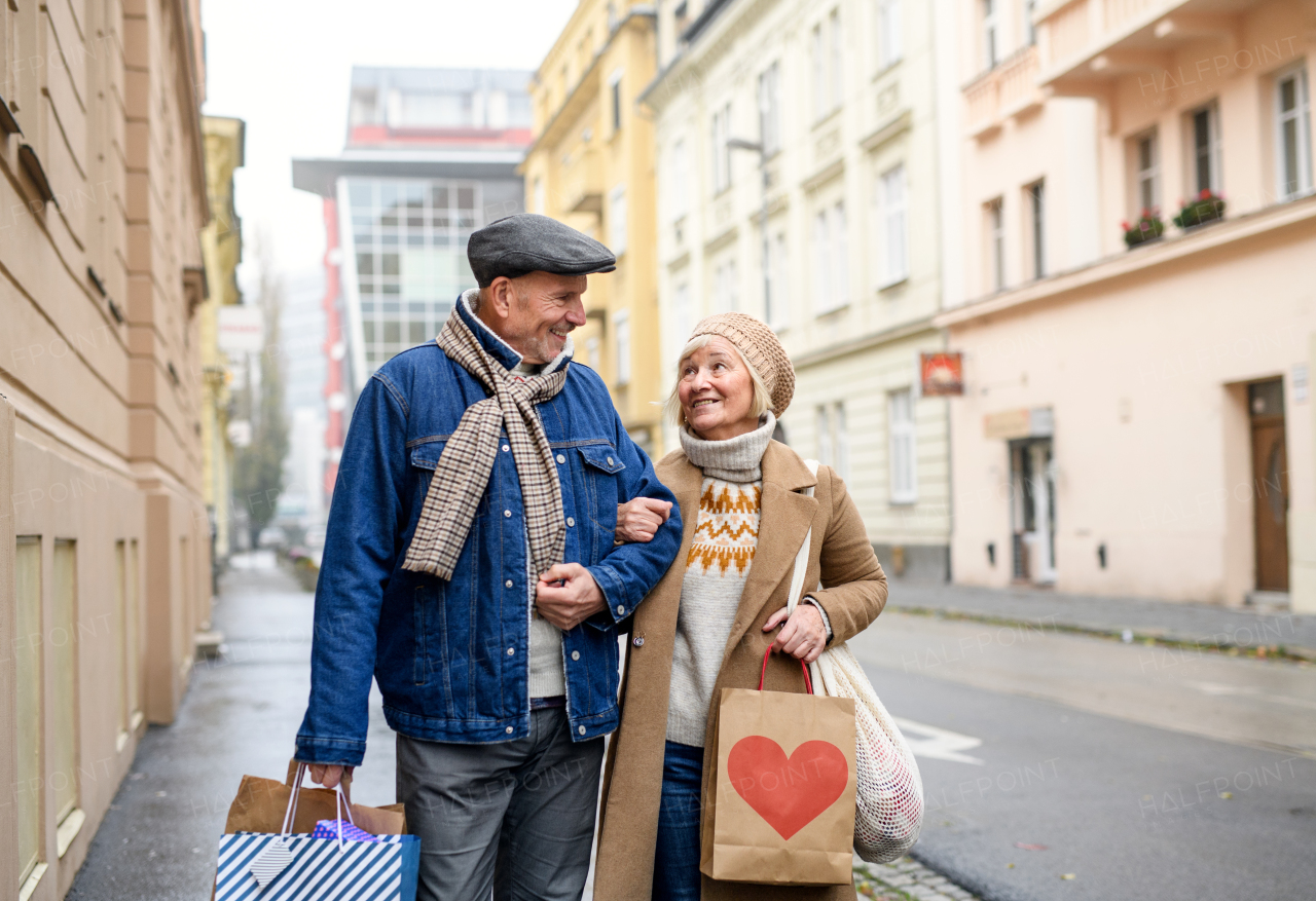 Portrait of happy senior couple walking outdoors on street in city, carrying shopping bags.