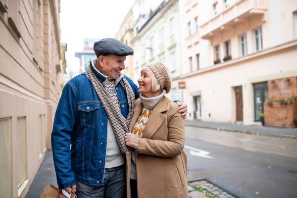 Portrait of happy senior couple walking outdoors on street in city, carrying shopping bags.