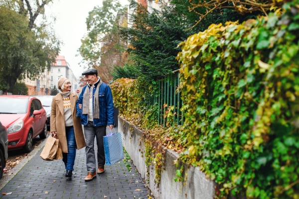 Portrait of happy senior couple walking outdoors on street in city, carrying shopping bags.