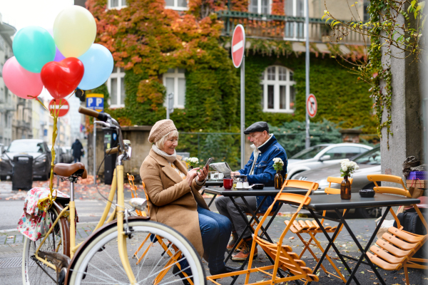 Happy senior people sitting in outdoor cafe in city, using smartphone.