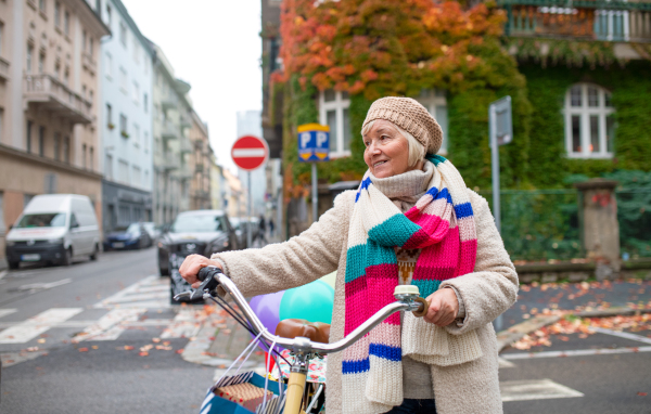 Portrait of senior woman with bicycle crossing road outdoors in city.