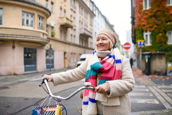 Portrait of senior woman with bicycle crossing road outdoors in city.