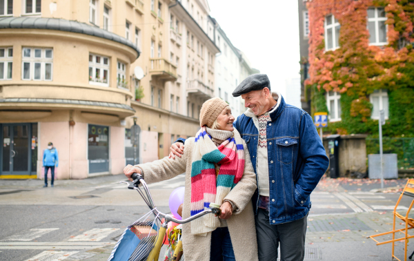 Happy senior couple with bicycle walking outdoors on street in city, carrying shopping bags and talking.