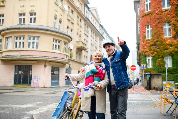 Portrait of happy senior couple with bicycle outdoors on street in city.