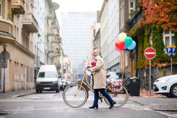 Portrait of senior woman with bicycle crossing road outdoors in city.