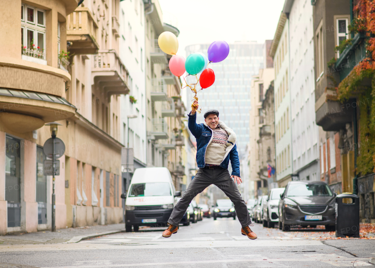 Happy senior man with balloons outdoors on street in city, jumping. Party concept.