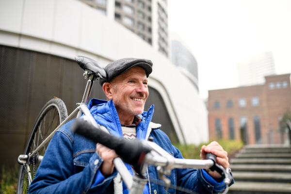 Portrait of happy senior man walking outdoors on street in city, carrying bicycle.