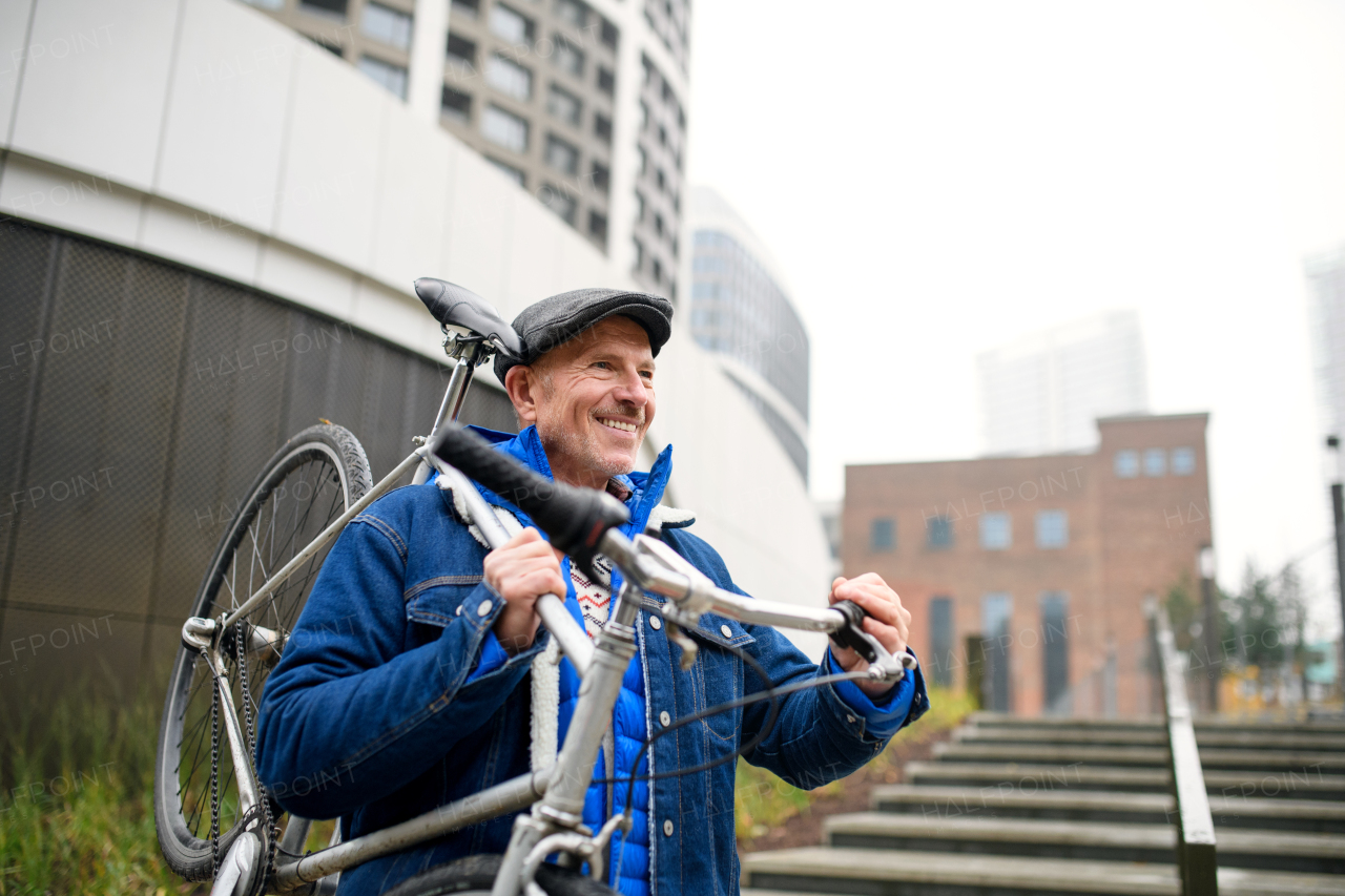 Portrait of happy senior man carrying bicycle outdoors in city.