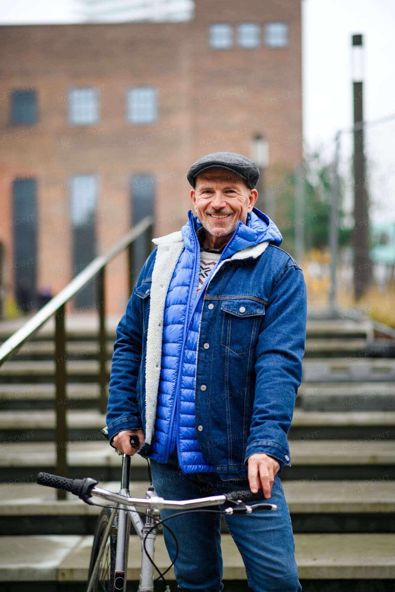 Happy senior man commuter with bicycle outdoors in city, looking at camera.