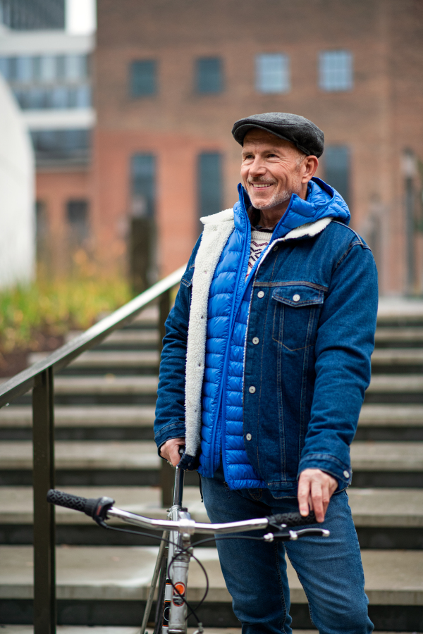 Happy senior man commuter with bicycle outdoors in city, standing.