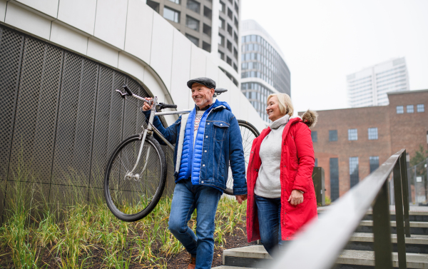 Portrait of happy senior couple with bicycle walking in city, holding hands.