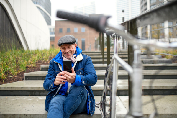 Portrait of happy senior man with bicycle outdoors in city, taking selfie.