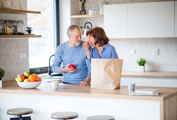 A portrait of happy senior couple indoors at home, unpacking shopping.