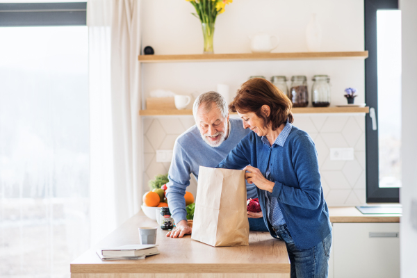 A portrait of happy senior couple indoors at home, unpacking shopping.