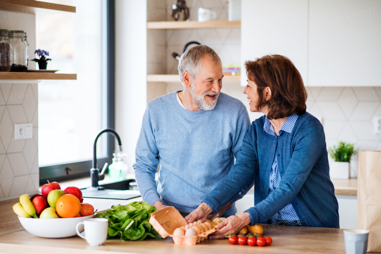 A portrait of happy senior couple indoors at home, unpacking shopping.