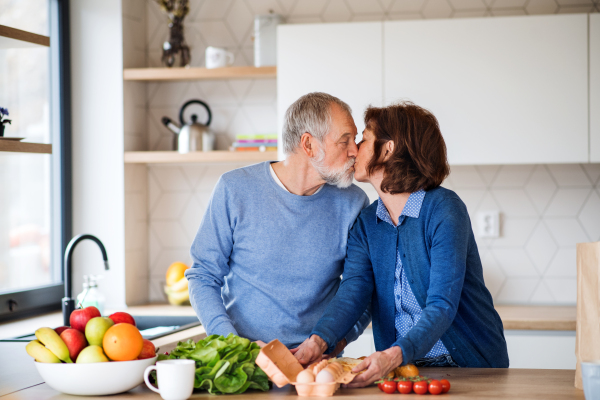 A portrait of happy senior couple in love indoors at home, kissing when cooking.