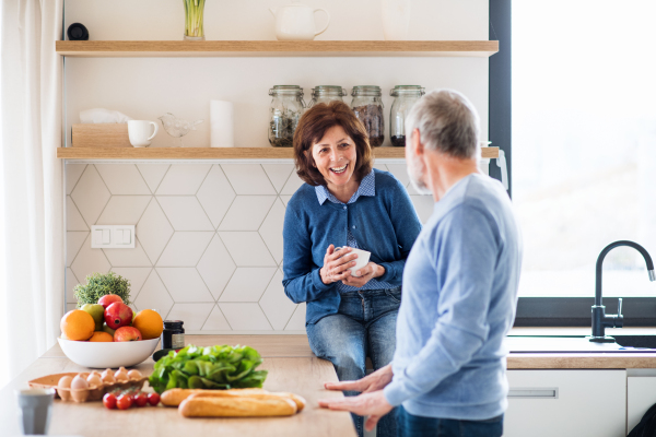 A portrait of happy senior couple with coffee indoors at home, talking.