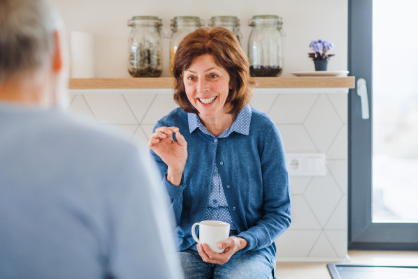 A portrait of happy senior couple with coffee indoors at home, talking.