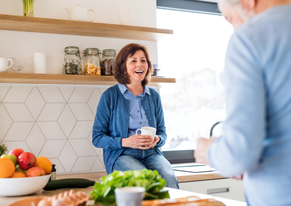 A portrait of happy senior couple with coffee indoors at home, talking.