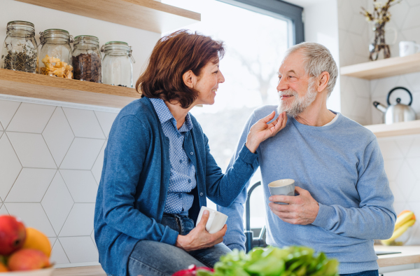 A portrait of happy senior couple in love indoors at home, holding coffee.