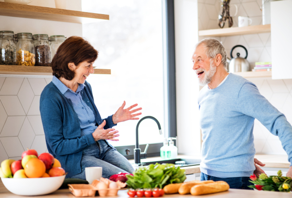 A senior couple in love indoors at home, man giving flowers to happy woman.