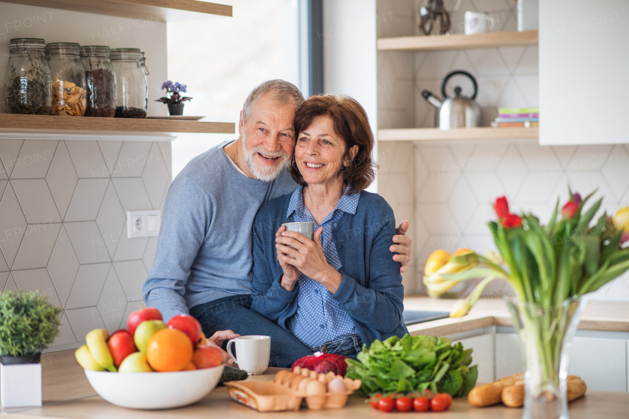 A portrait of happy senior couple in love indoors at home, holding coffee.