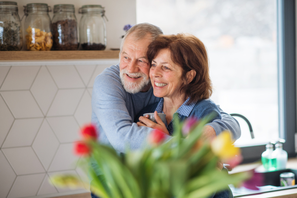 A portrait of happy senior couple in love indoors at home, holding coffee.