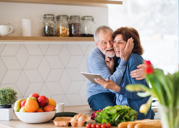 A portrait of happy senior couple in love indoors at home, looking for recipe using tablet.